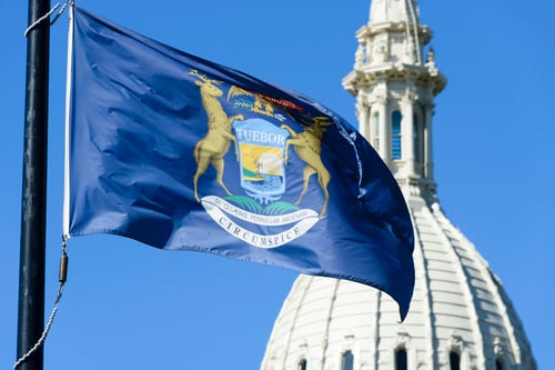 Michigan state flag waving in front of the capitol