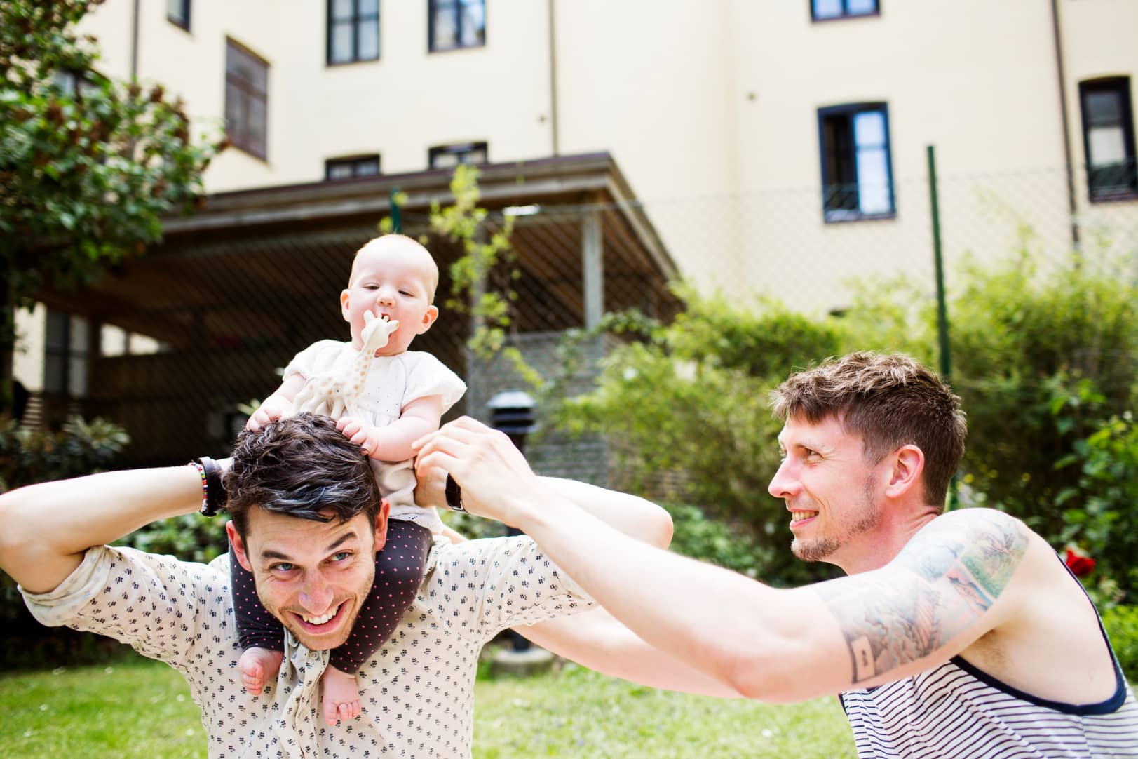 cheerful-gay-men-playing-with-baby-girl-at-yard-9B62NEJ